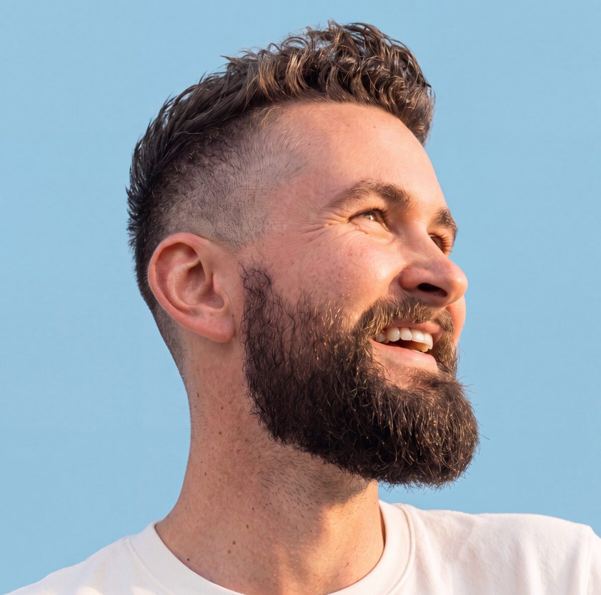 Man with fade haircut and groomed beard, smiling to the right.